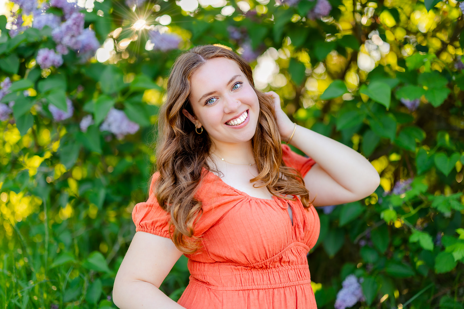 A happy high school senior pulls her hair back while standing in a flowering garden at sunset