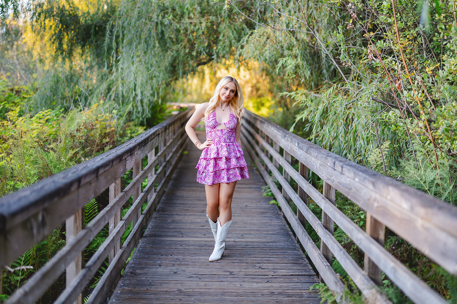 a high school senior in a pink dress walks on a boardwalk with a hand on her hip after shopping for Homecoming Dresses Seattle