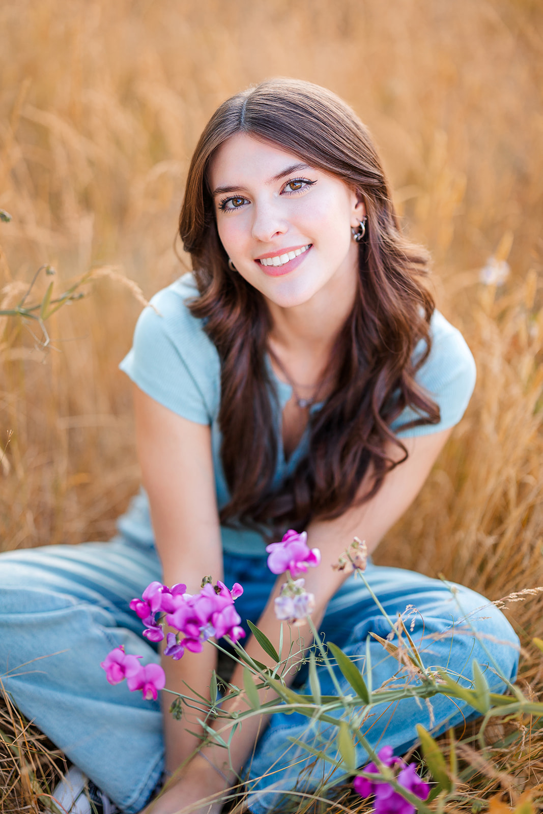 A Liberty High School Washington senior sits in tall golden grass smiling with legs crossed