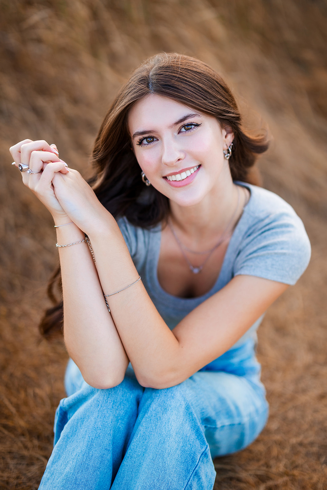 A smiling high school senior sits in jeans in golden grass at sunset after visiting Nail Salons Renton, WA