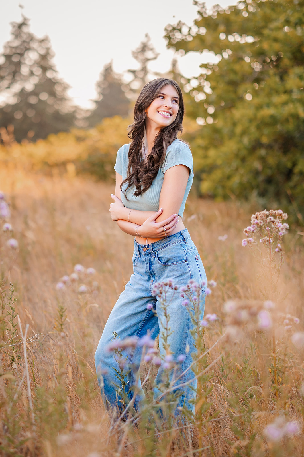 A woman in jeans and a blue top smiles while hugging herself after attending Newport High School