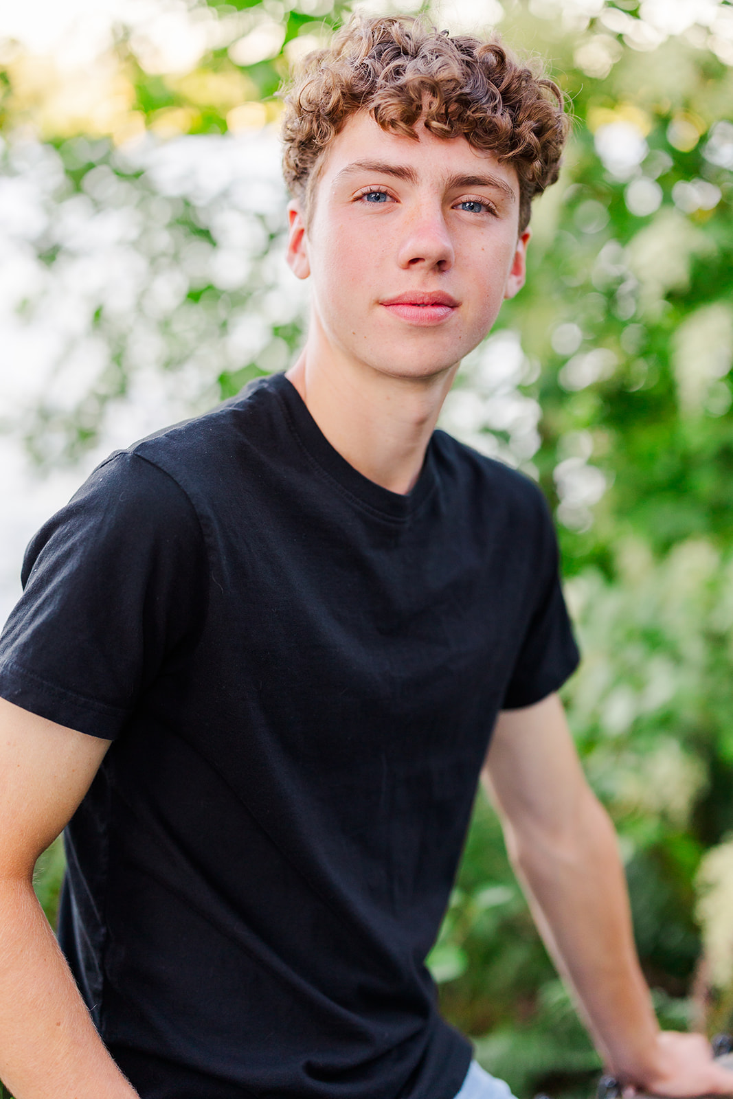 A Sammamish High School senior in a black shirt sits on a garden fence at sunset