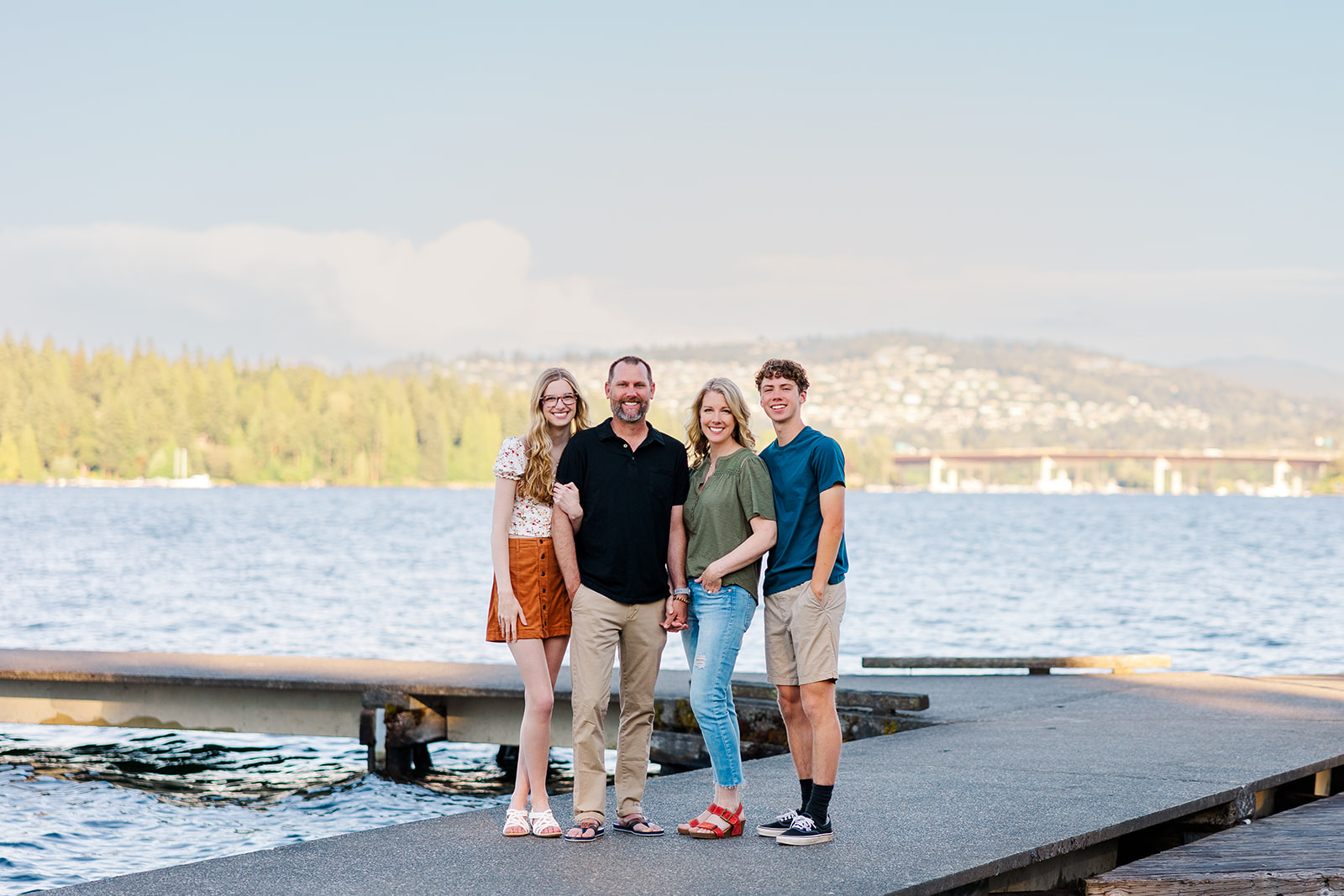 Happy mom and dad stand on a dock holding hands with their two Sammamish High School students