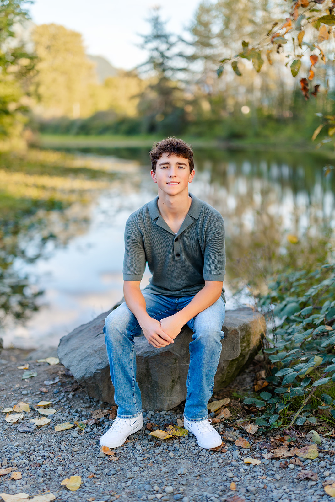 A smiling man in a polo and jeans sits on a rock on a river after using SAT Prep Issaquah