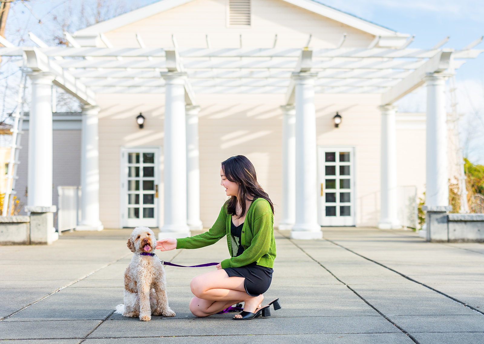 A woman in a black dress and green sweater pets her white dog on a patio after some SAT Prep in Seattle