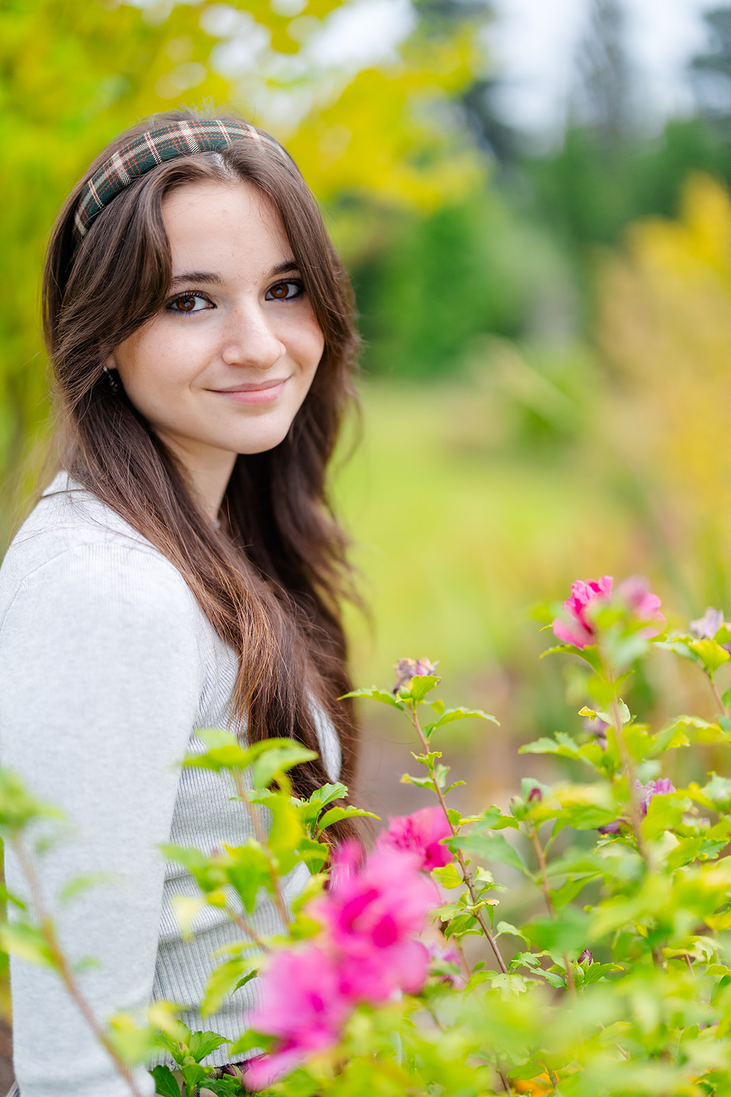 A smiling high school senior stands among some pink flowers in a garden