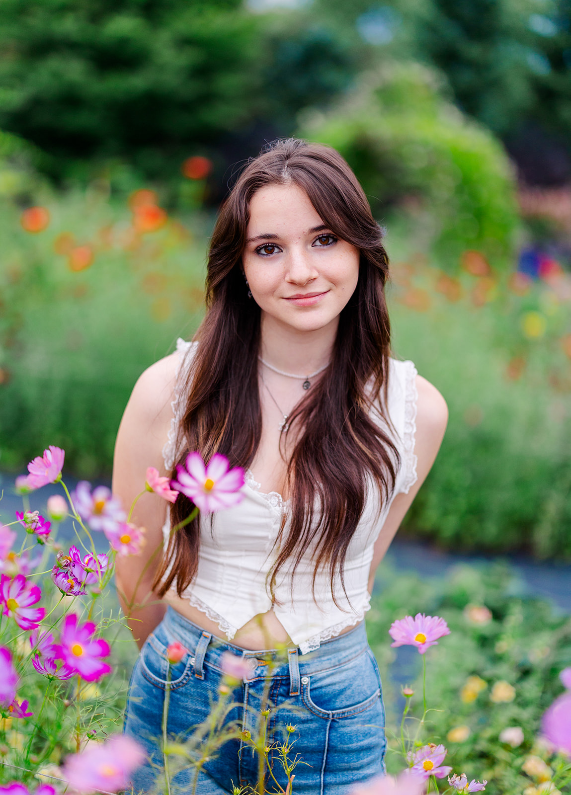 A high school senior in a white top stands among purple flowers in a garden before visiting Seattle Nail Salon