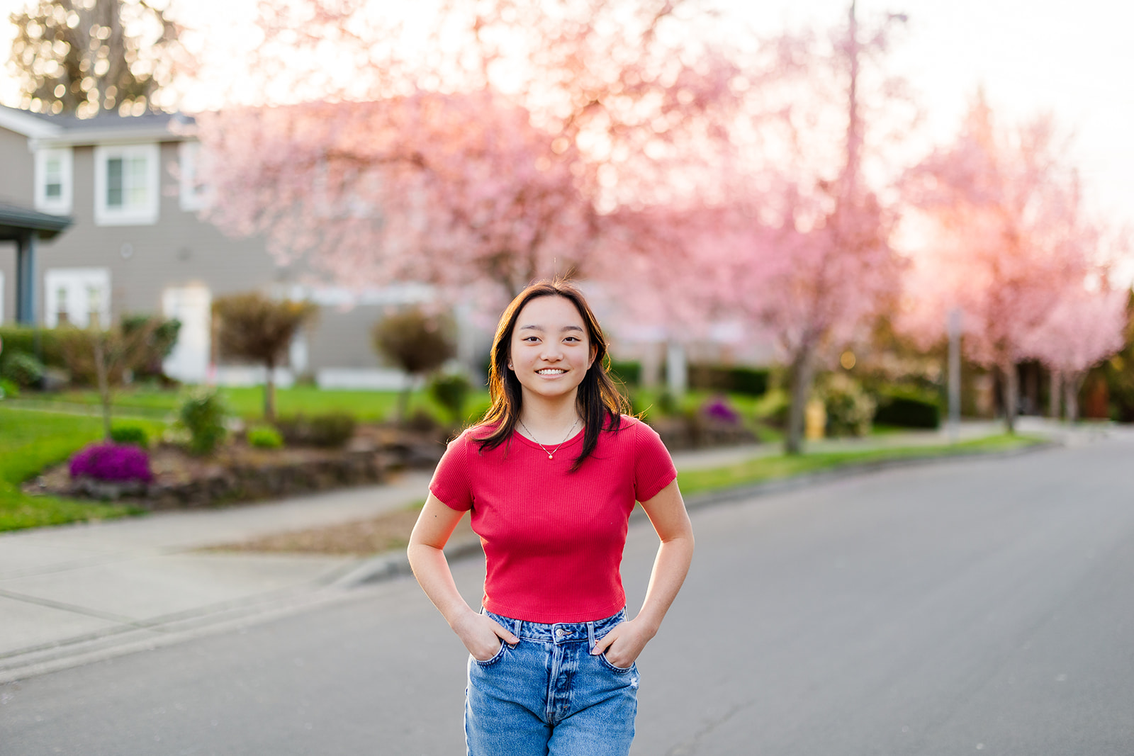 A woman in a red shirt and jeans stands in a suburb street smiling at sunset after attending Seattle Private Schools