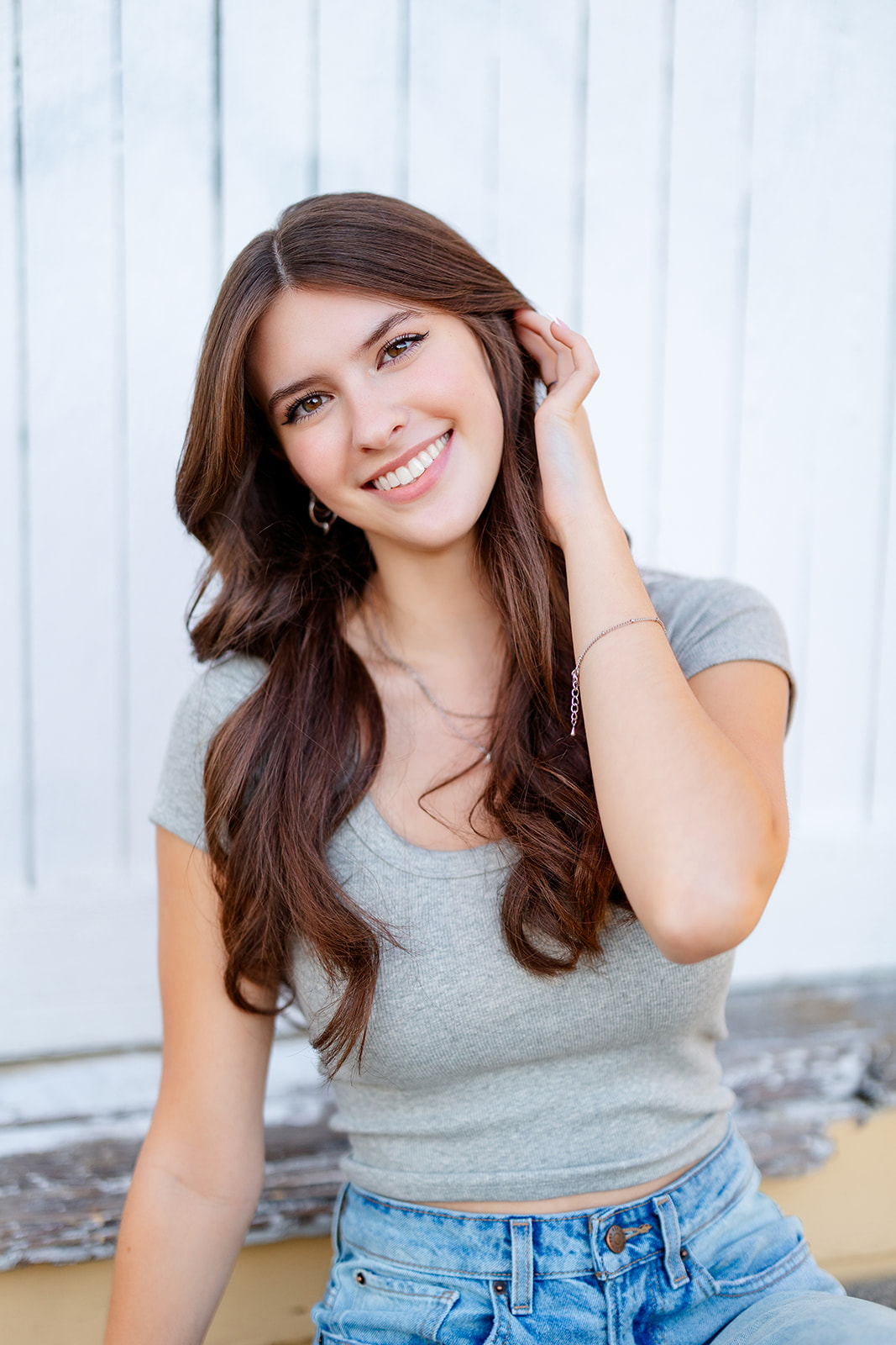 A high school senior sits against an old wall pulling her hair back behind her ear before visiting a Seattle Tanning Salon