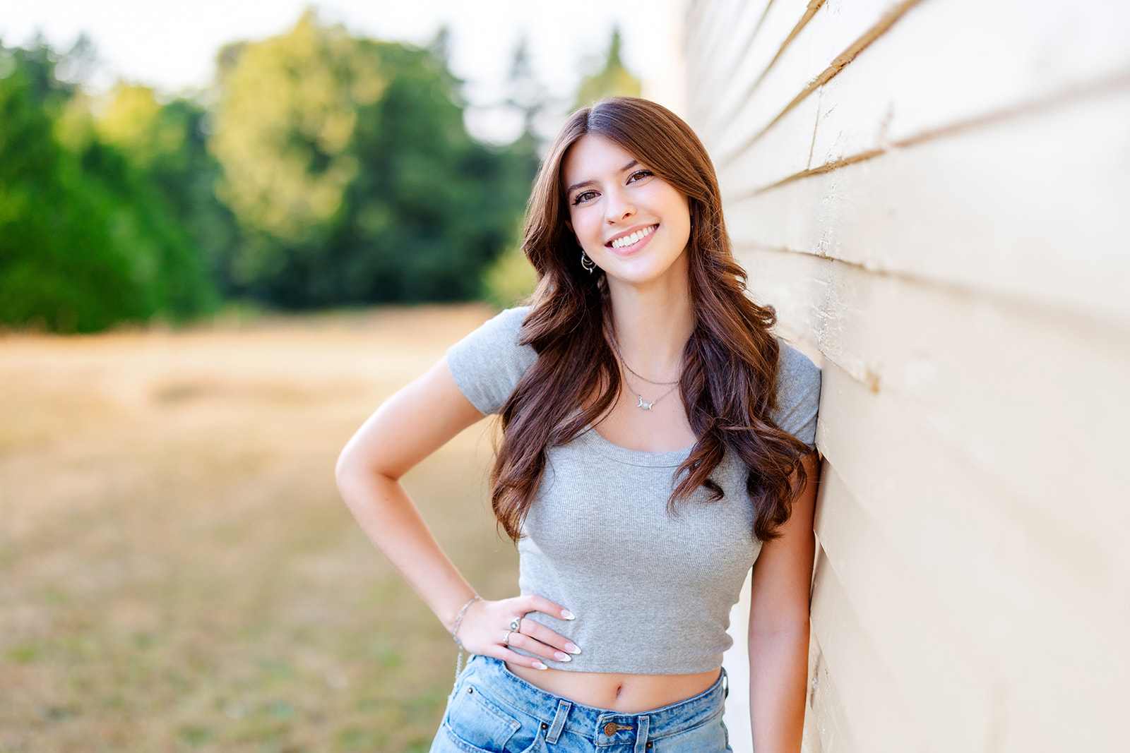 A woman in a grey shirt leans on a wooden wall before visiting a Seattle Tanning Salon