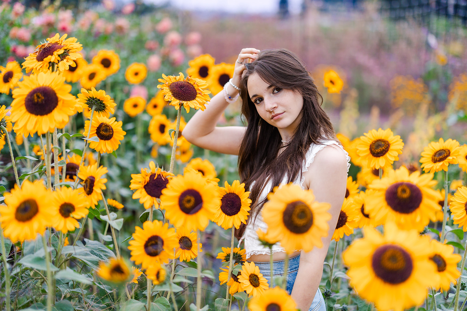 A Skyline High School Washington senior stands among sunflowers in a white top with a hand in her hair