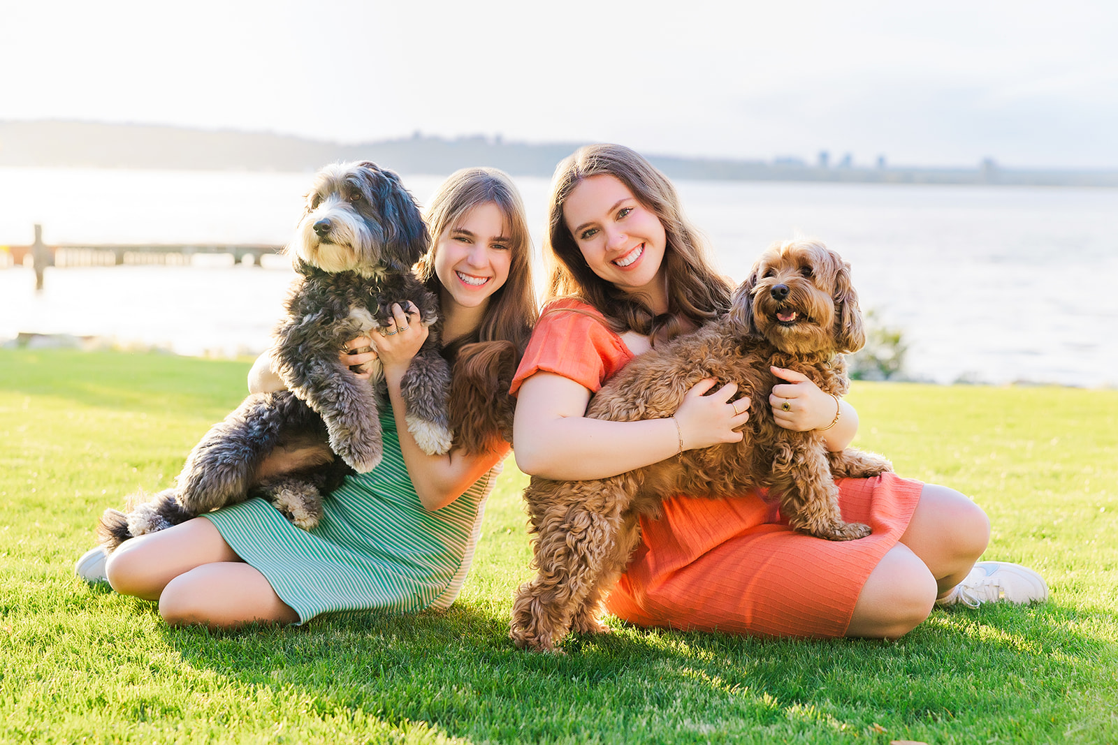 Two Skyline High School Washington seniors sit in a waterfront lawn holding their two dogs in their laps