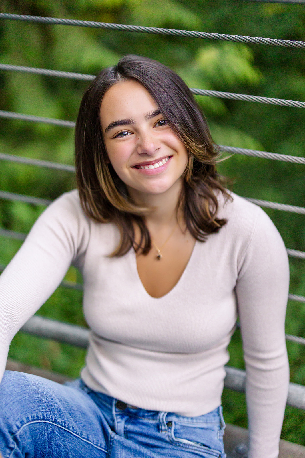 A happy high school senior sits against a bride guard rail in a white top and jeans