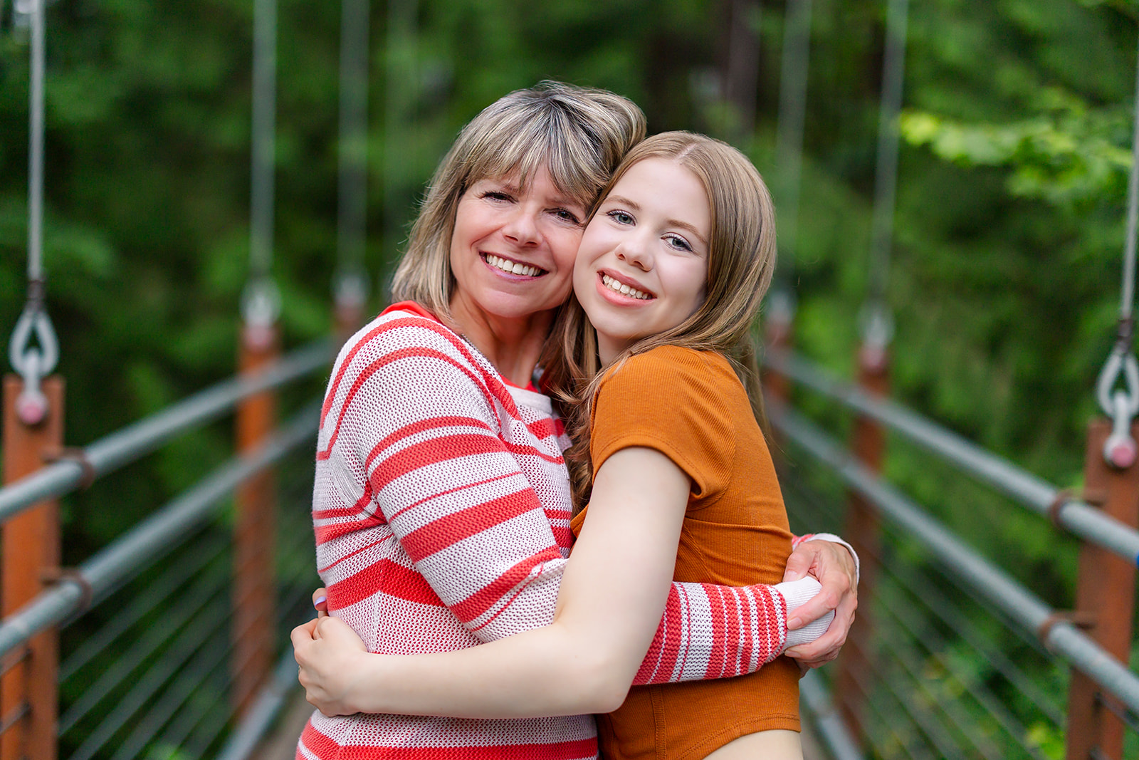 A happy mom in a red sweater hugs her high school senior daughter on a foot bridge before visiting Tanning Salons Renton, WA