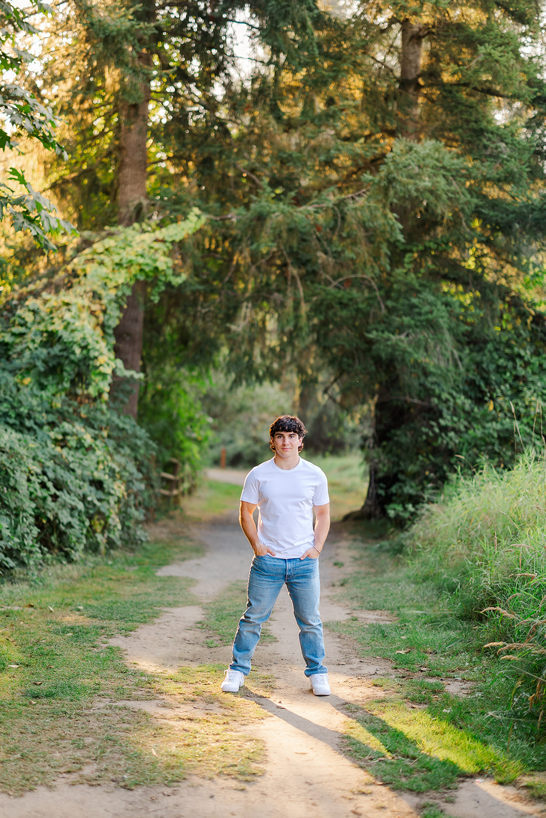 A teenage boy stands in a park trail at sunet with hands in his jean pockets