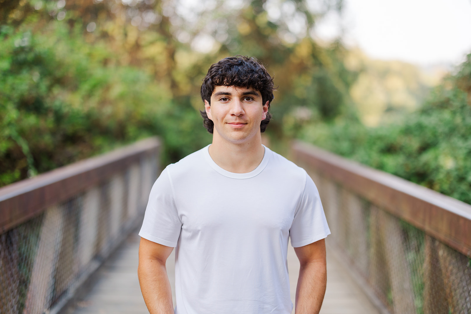 A high school senior in a white shirt smiles while walking across a bridge after visiting the Jewish Community Center Mercer Island