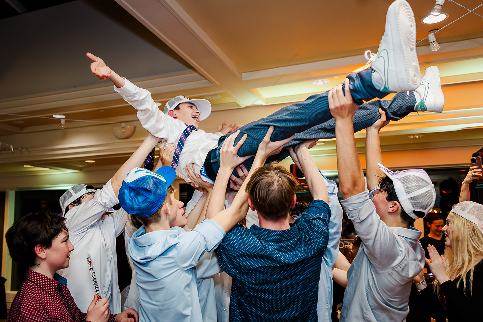 A teen is lifted in the air by his friends in a ballroom