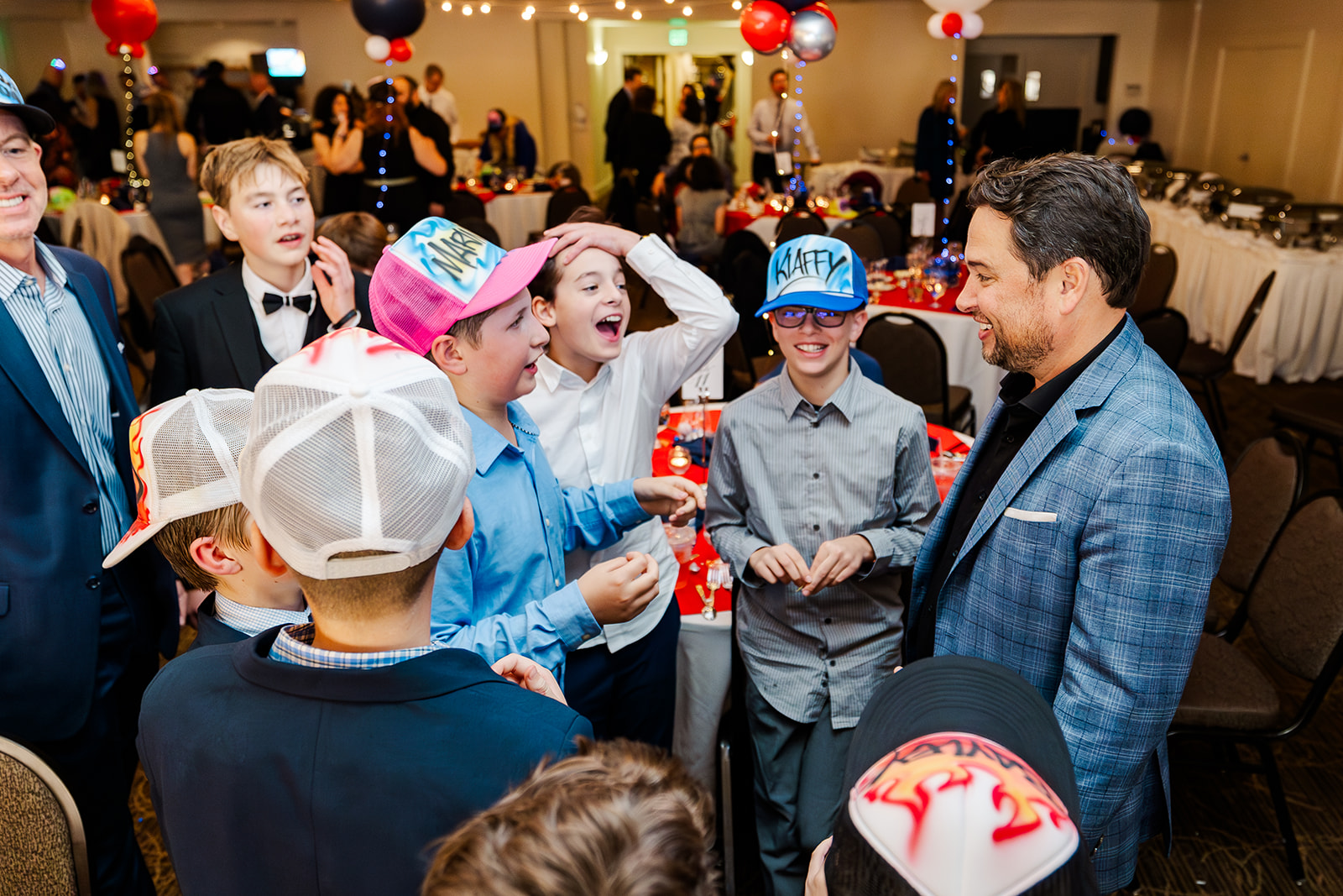 A group of boys in matching hats chat with a man in a blue suit at a Mitzvah catered by Down To Earth Cuisine