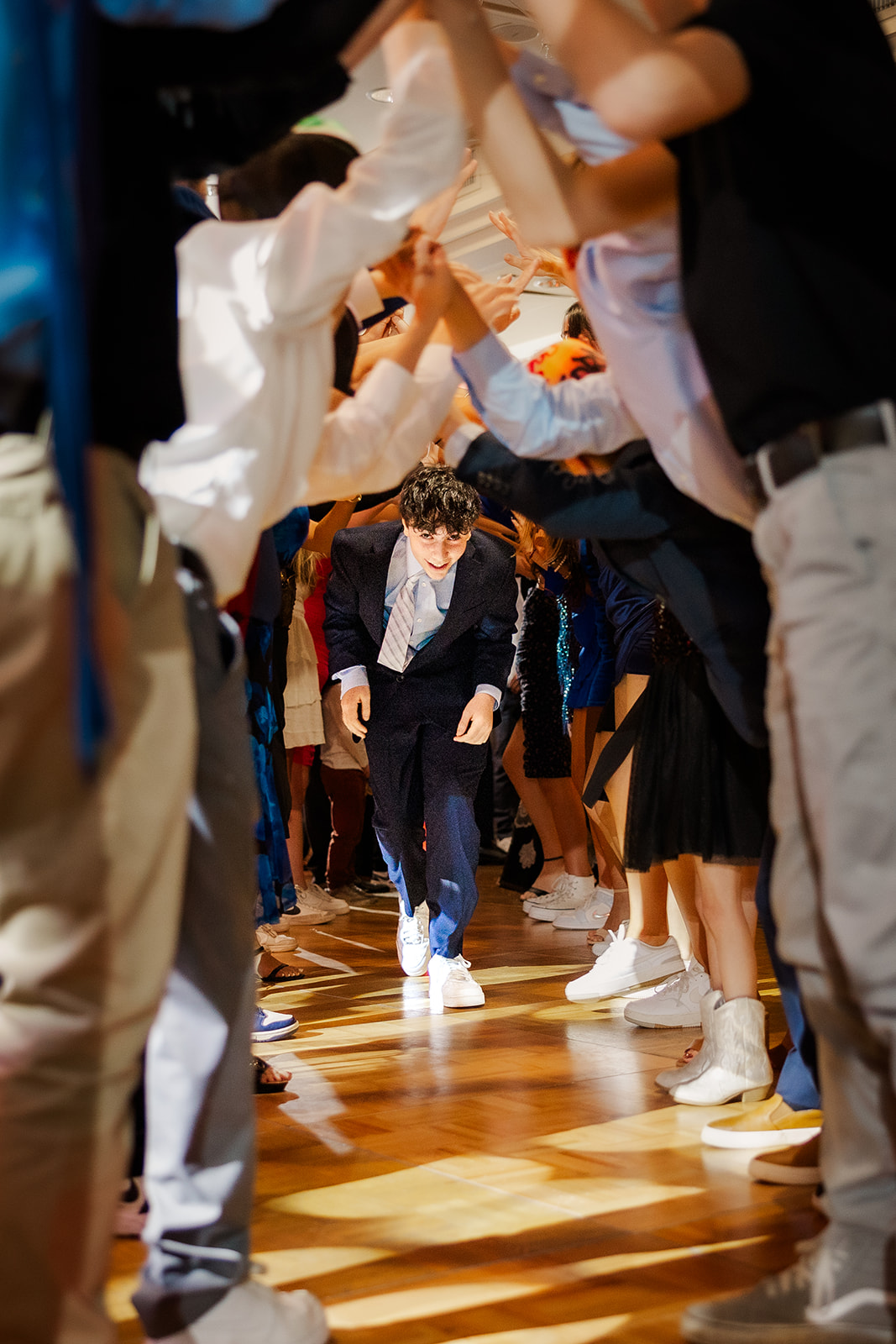 A teen in a blue suit runs under an archway of arms of friends on the dance floor at event venues in Bellevue, WA