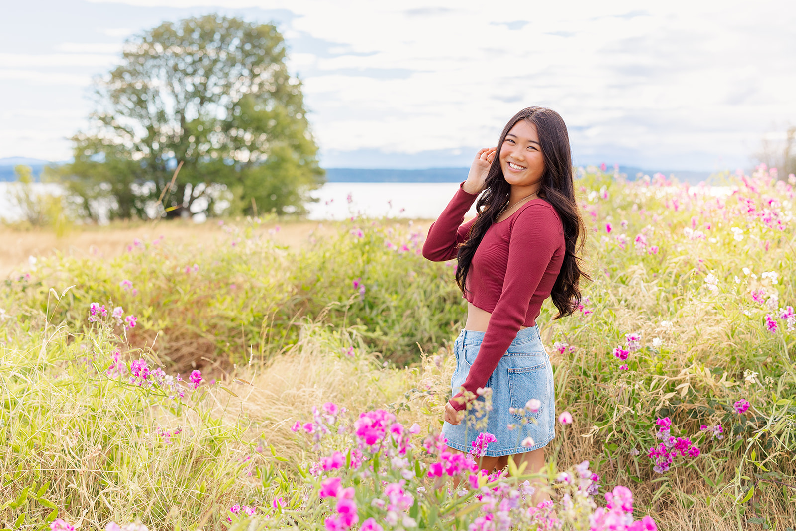 A high school senior walks through a field of wildflowers in a maroon top and jean skirt