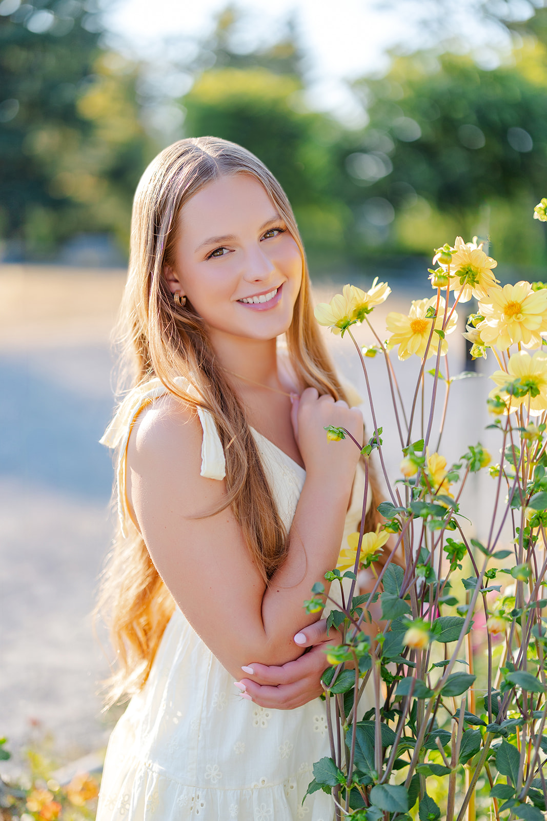 A high school senior stands by some yellow flowers in a garden in a matching dress after visiting florists in Renton, WA