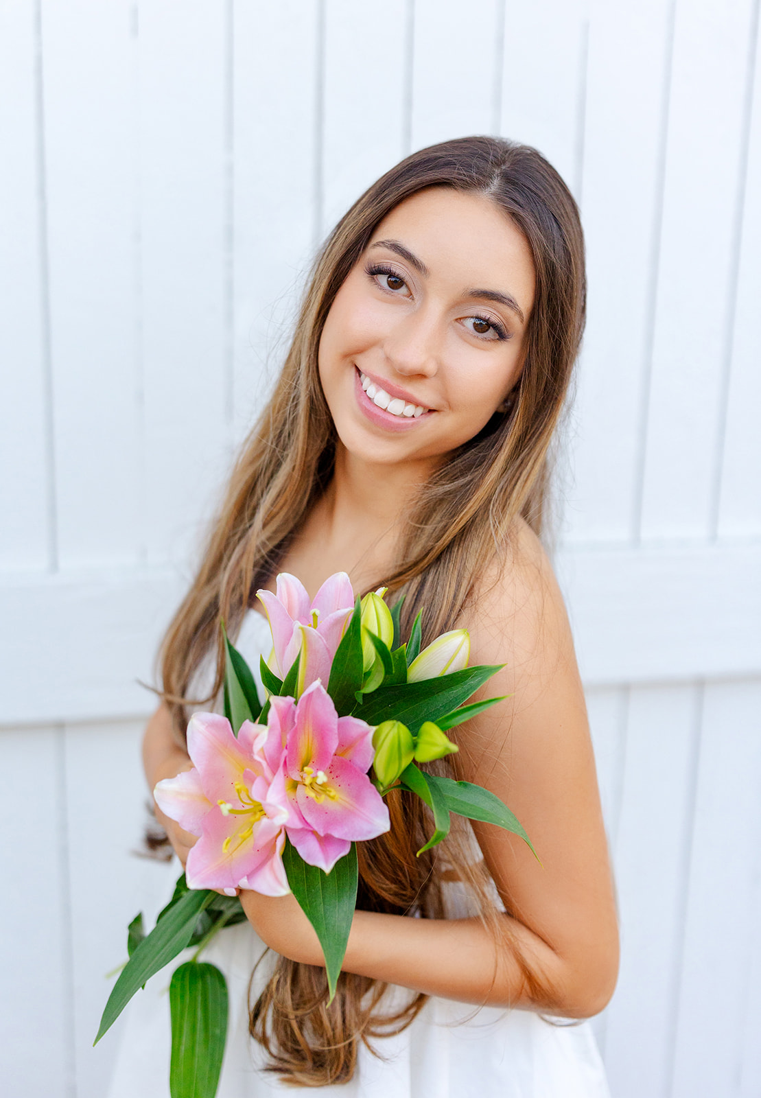 A woman in a white dress stands by a fence holding pink flowers from florists in Renton, WA