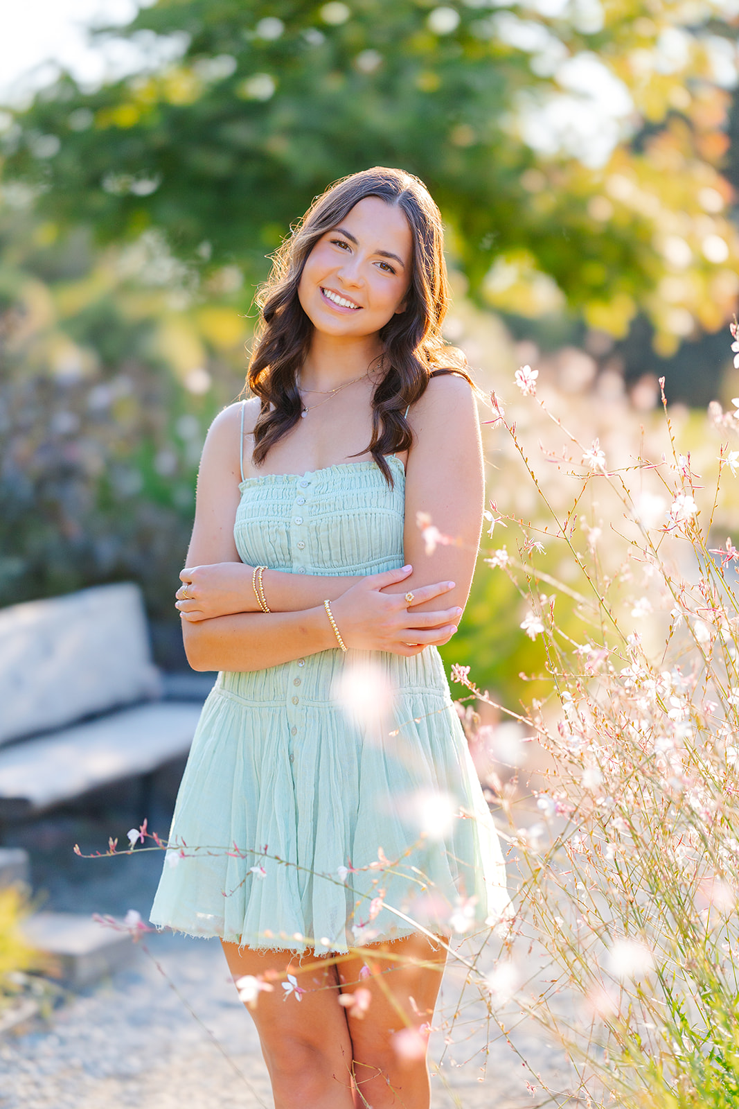 A high school senior crosses her arms in a green dress while exploring a garden at sunset after visiting makeup artists in Issaquah, WA