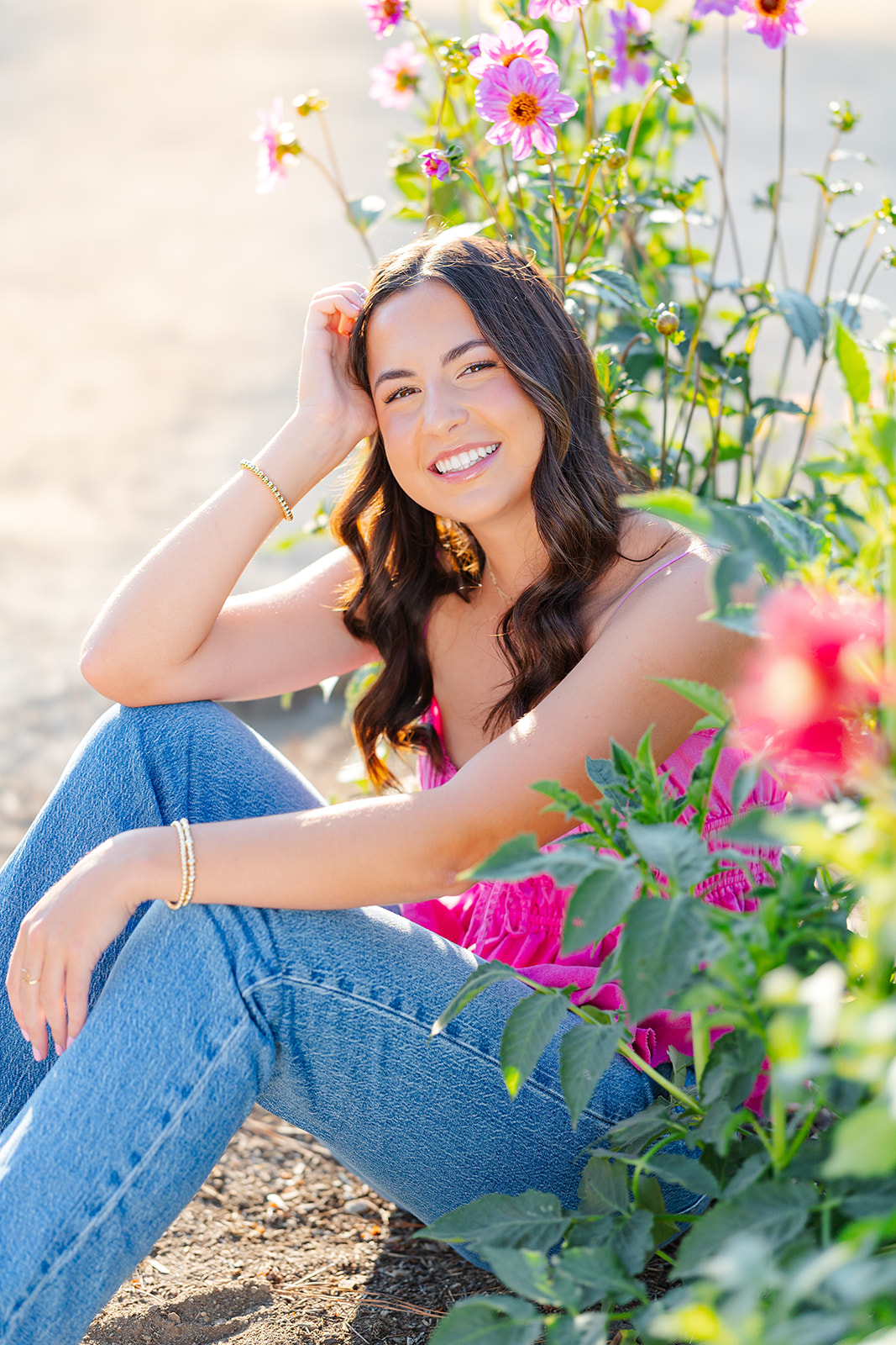 A high school senior sits among pink flowers smiling after visiting makeup artists in Issaquah, WA