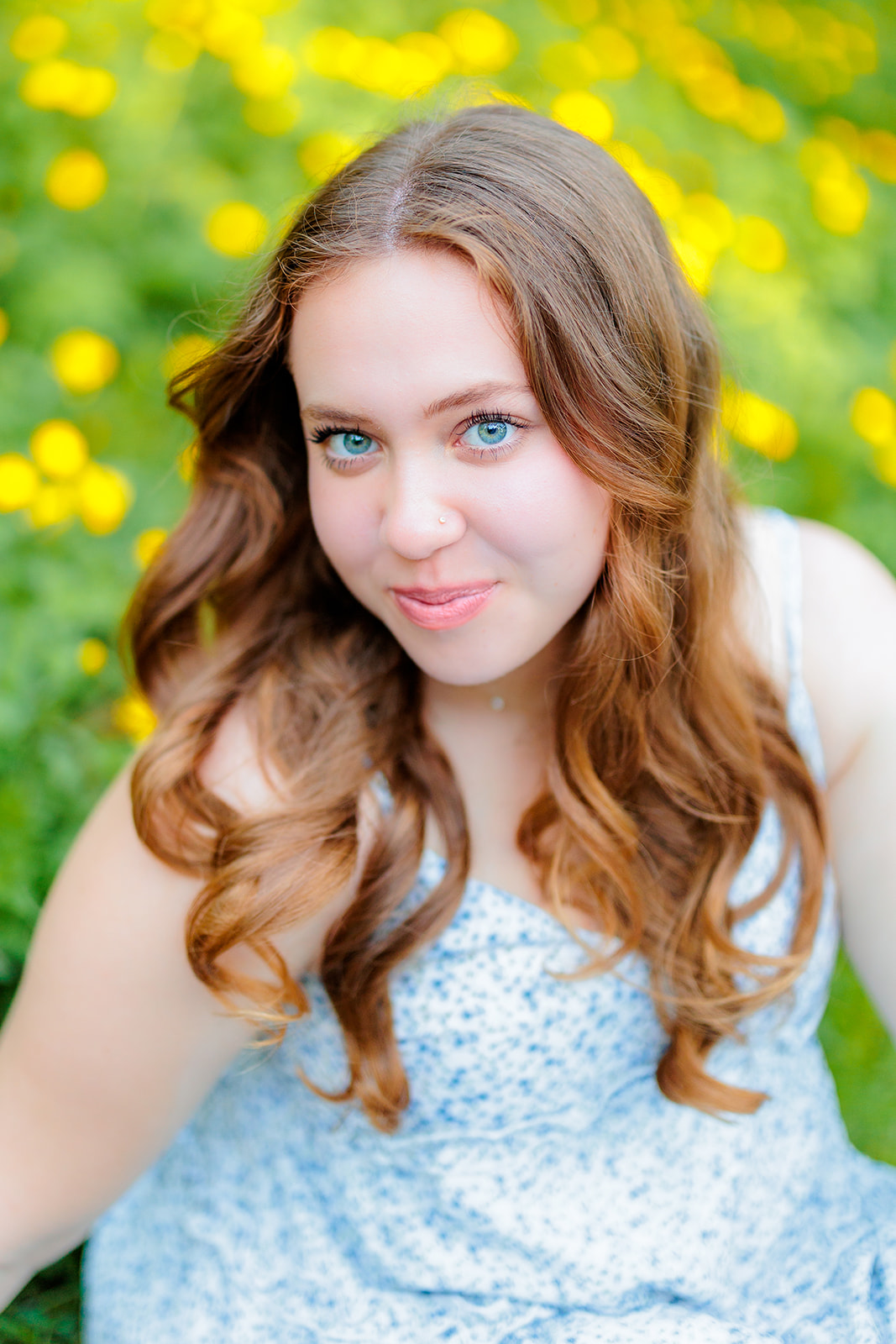 A teen girl in a blue dress smirks while sitting among yellow flowers in a blue dress