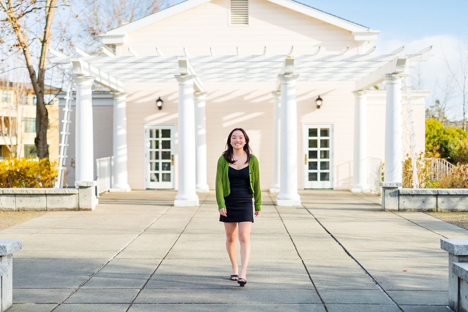 A high school senior walks in a garden by a pergola in a black dress after using makeup artists in Renton, WA