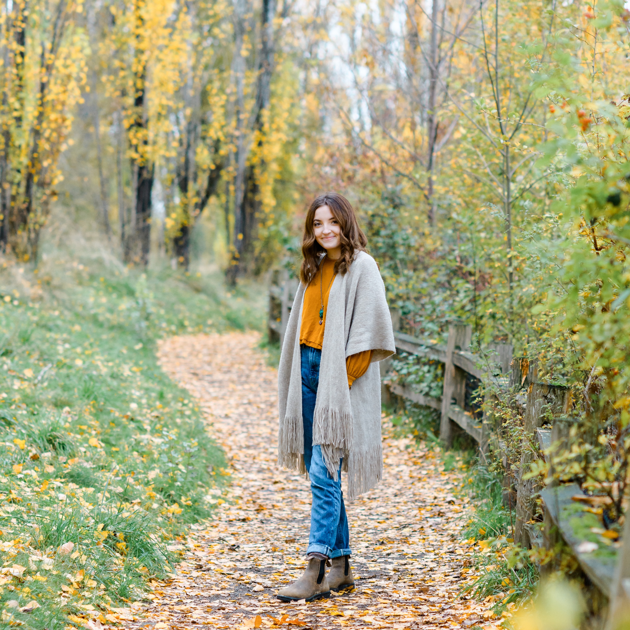 A Bellevue Christian School senior in a grey jacket and jeans walks in a park trail with hands in pockets