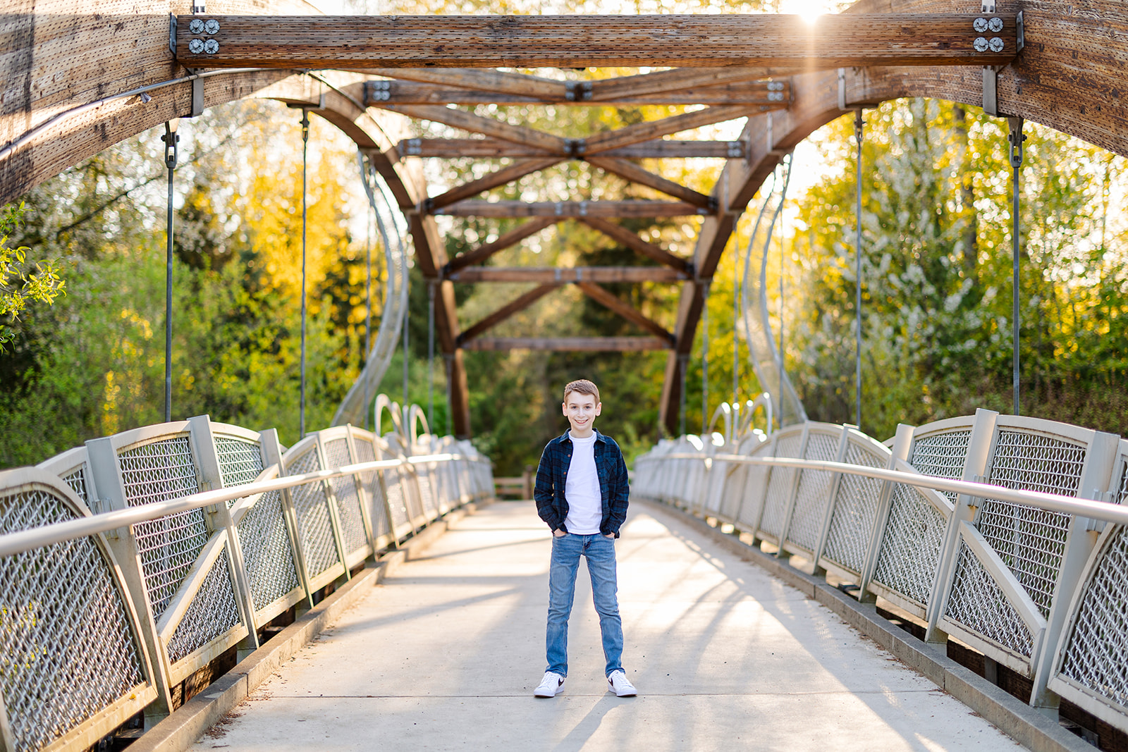 A young boy stands on a park bridge with hands in his jean pockets with a blue plaid shirt after exploring Catering in Issaquah