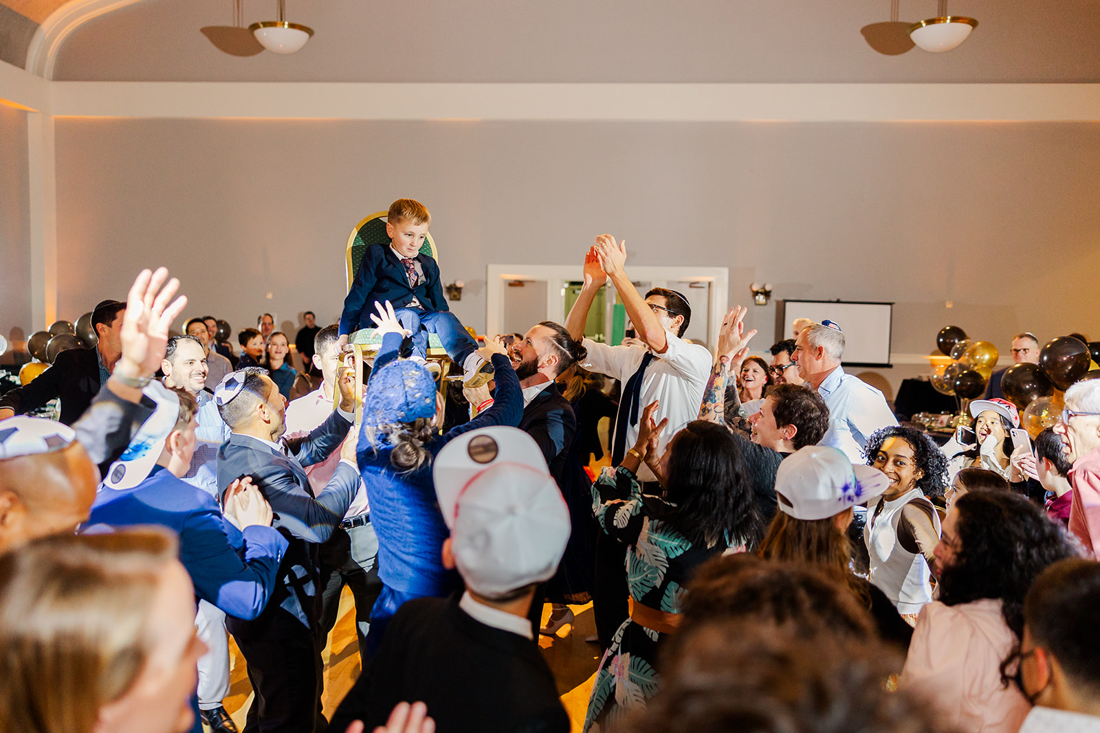 A young boy sits in the gold chair while being lifted in the center of the dance floor
