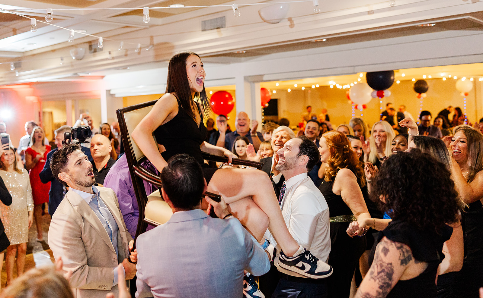 A happy teen girl in a black dress celebrates in a lifted chair on the dance floor thanks to a DJ in Kirkland, WA