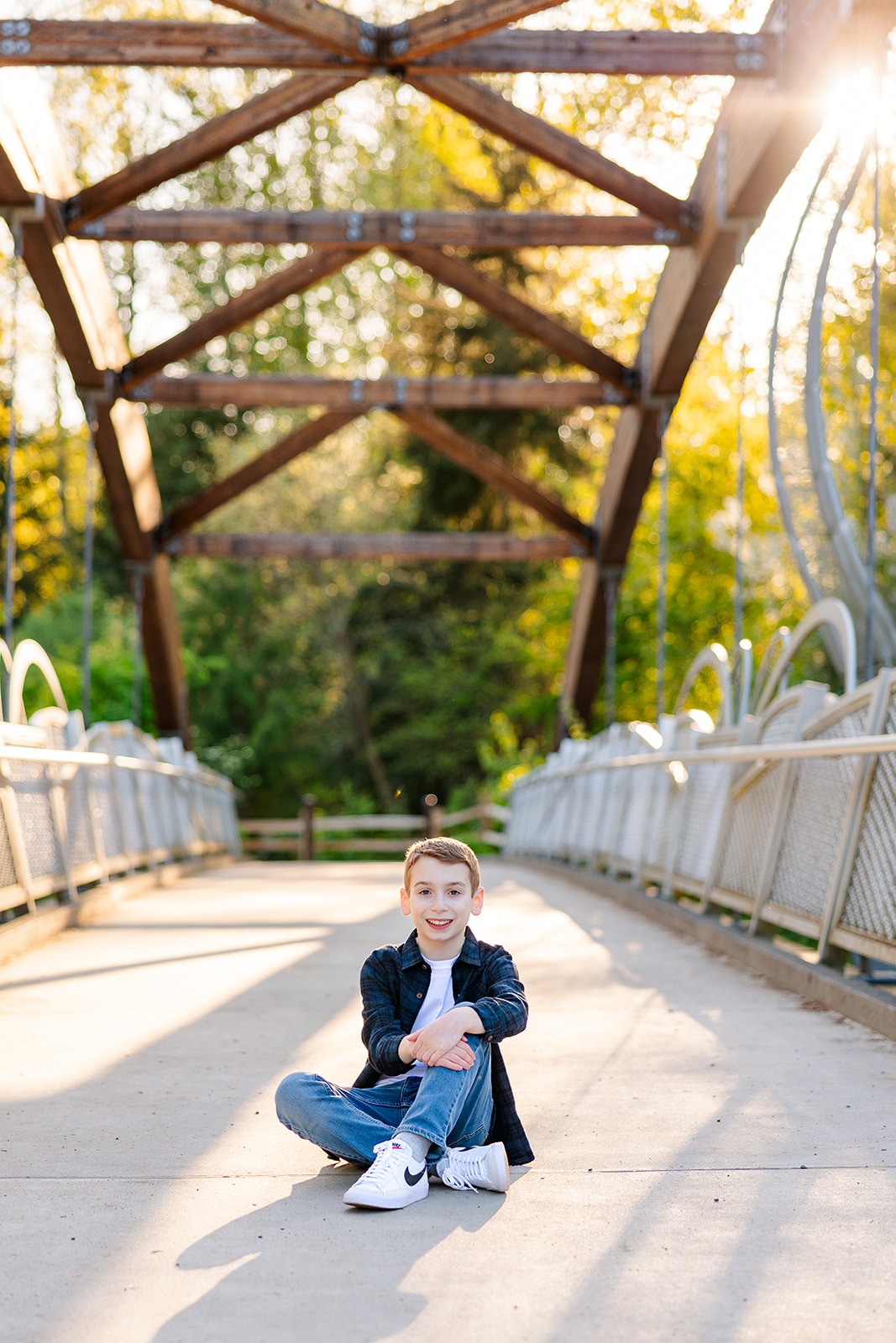 A young boy in jeans sits in a pedestrian bridge at sunset