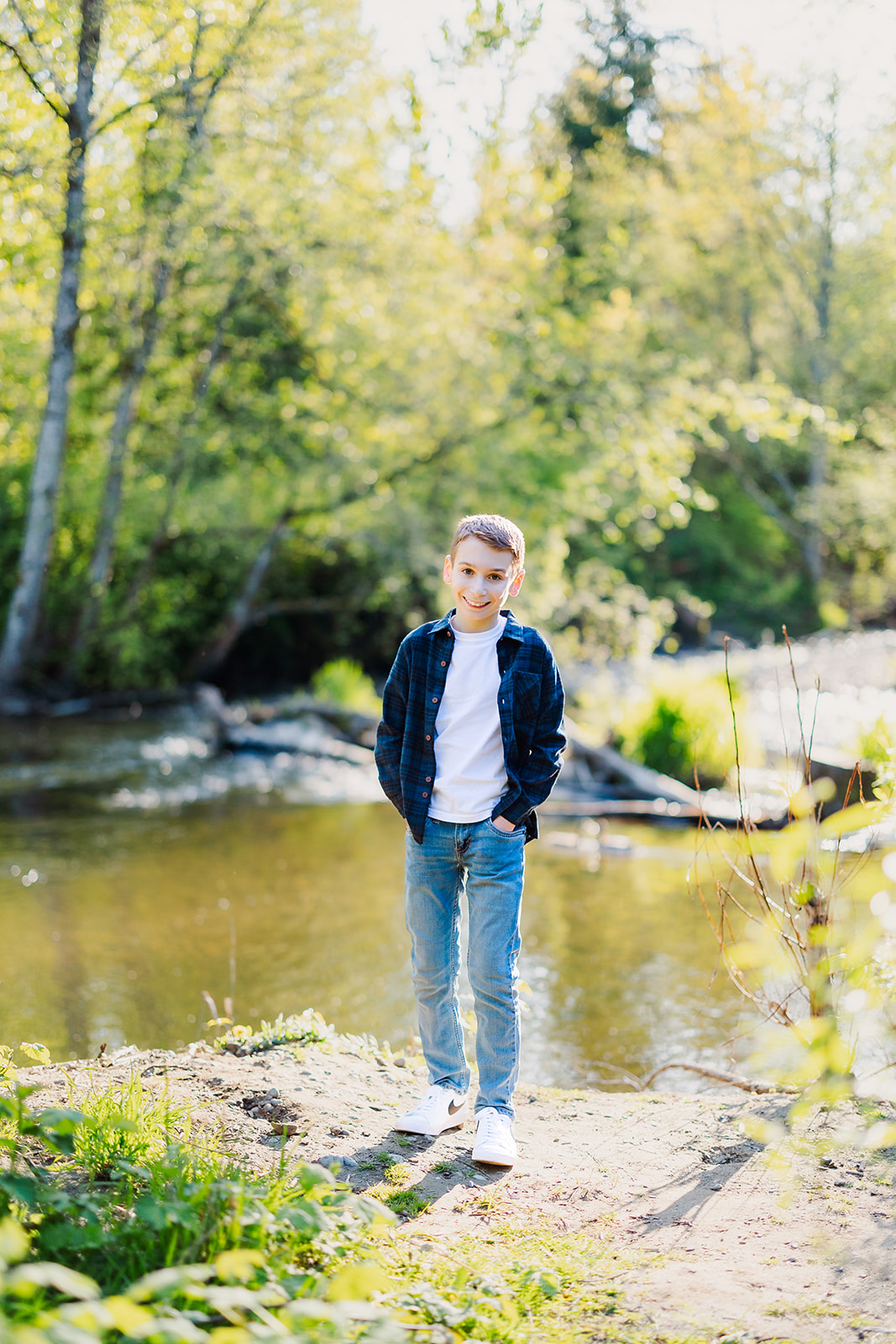 A young boy in jeans and plaid smiles while standing by the water after finding event planners in Seattle