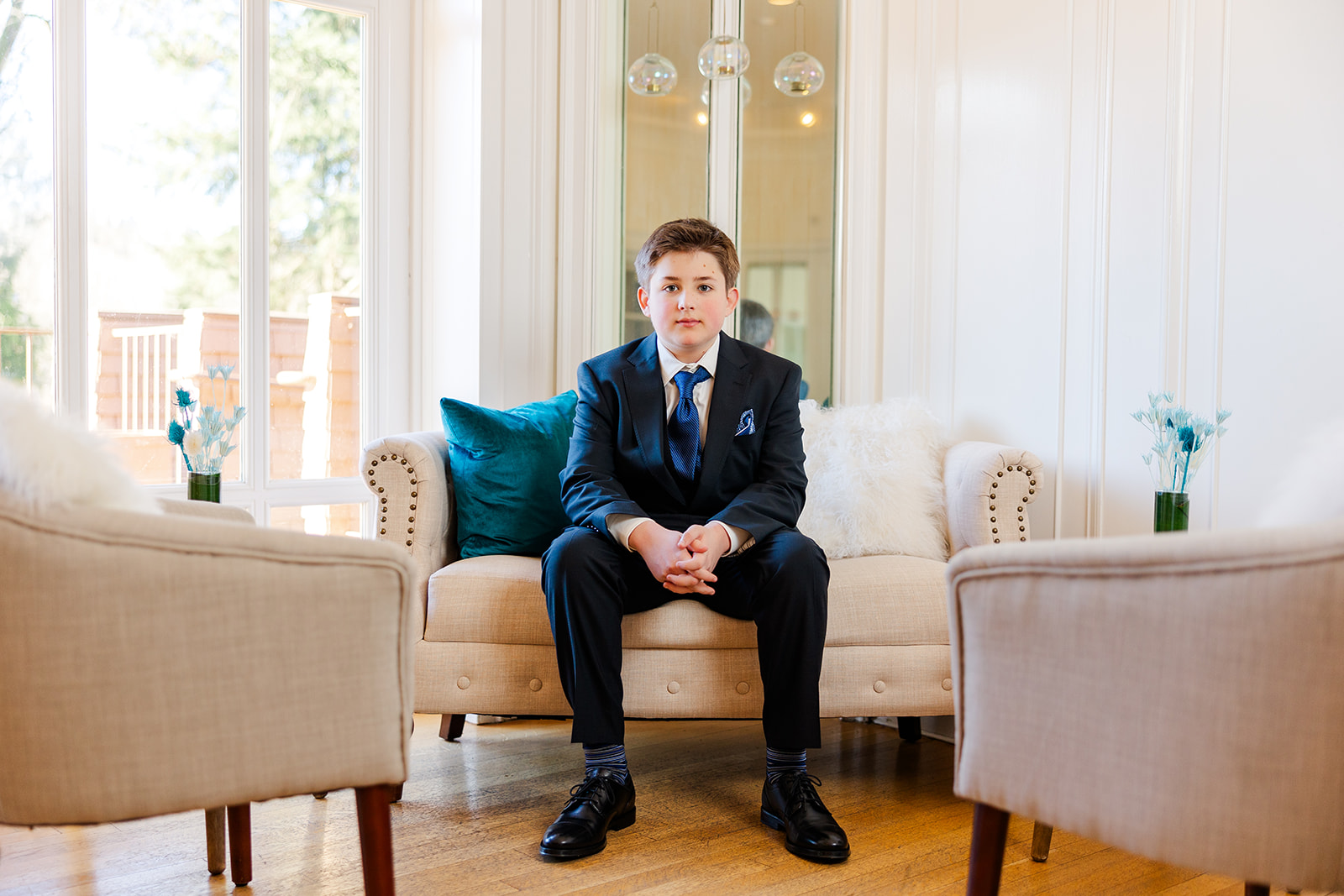 A young boy in a blue suit sits on a modern couch leaning on his knees after finding Issaquah party rentals