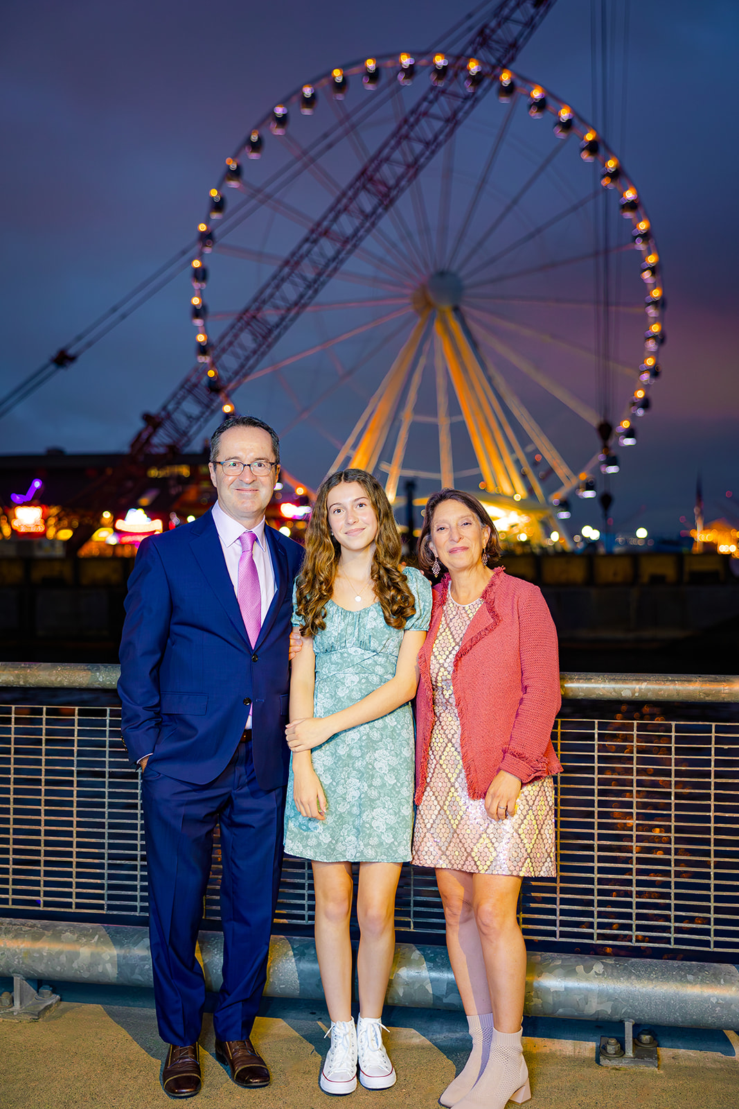 Proud mom and dad stand with the ferris wheel in the background with their daughter at Kirkland Event Spaces