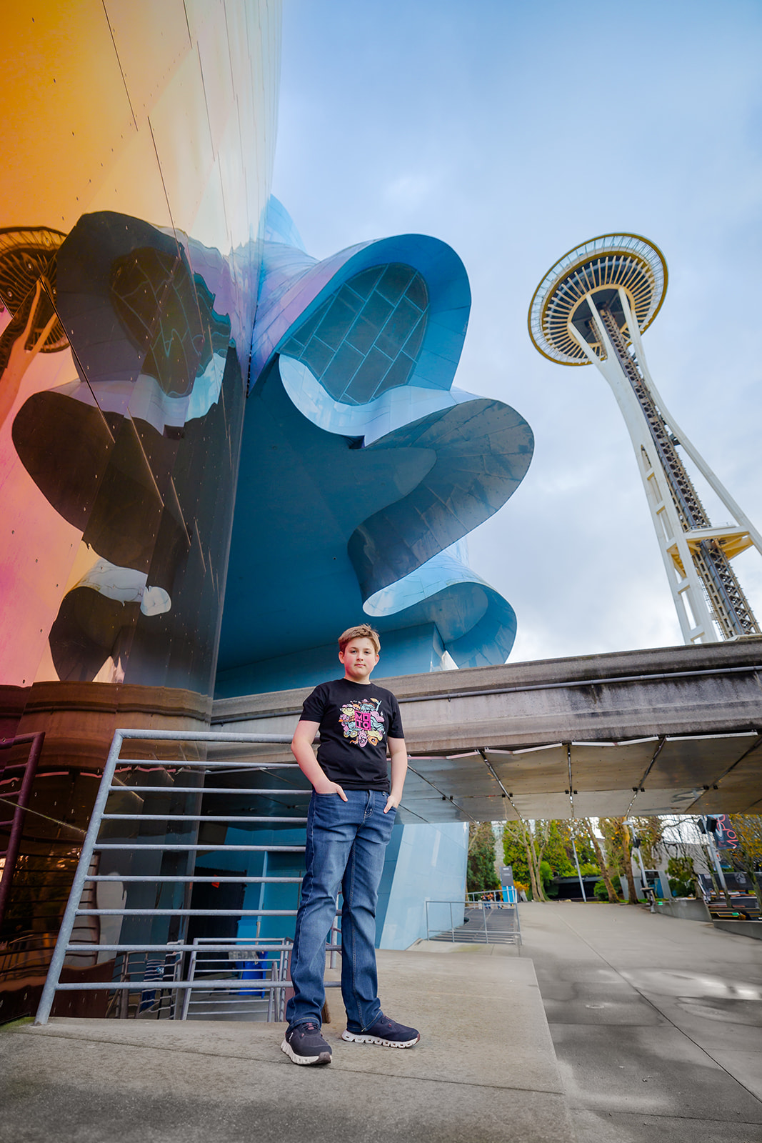 A teen boy in a black shirt and jeans stands under the space needle