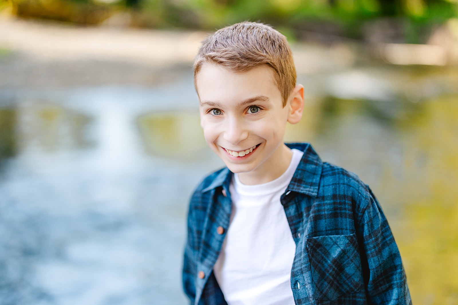 A happy young boy walks with a big smile by the water in a blue shirt