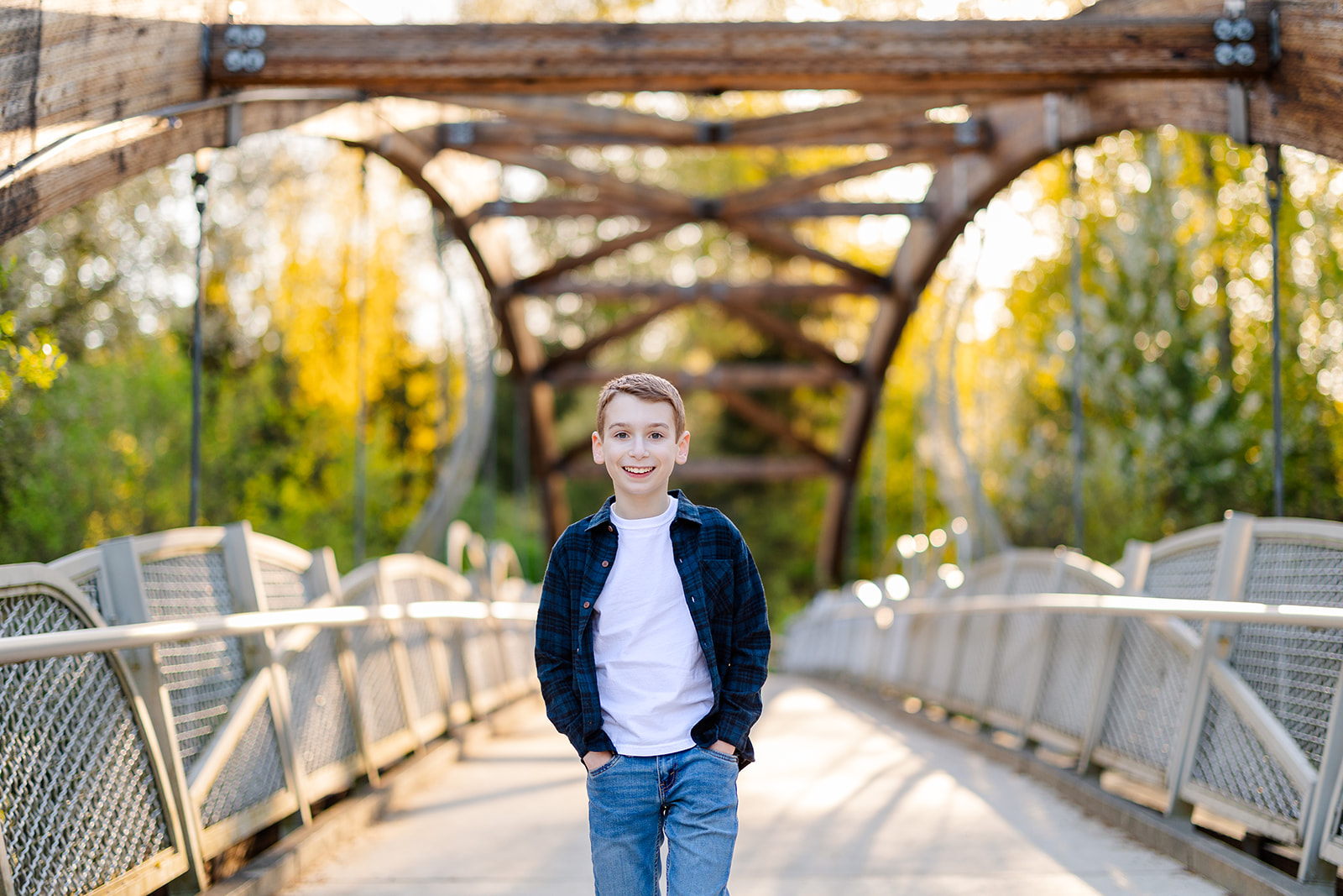 A happy young boy in blue flannel and jeans walks with hands in pockets on a pedestrian bridge after exploring party rentals in Kirkland