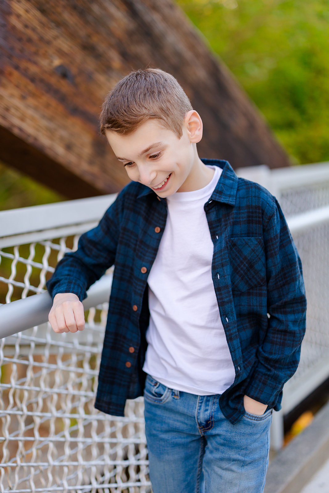 A young boy smiles while leaning on a bridge railing in blue plaid and jeans after exploring party rentals in Kirkland