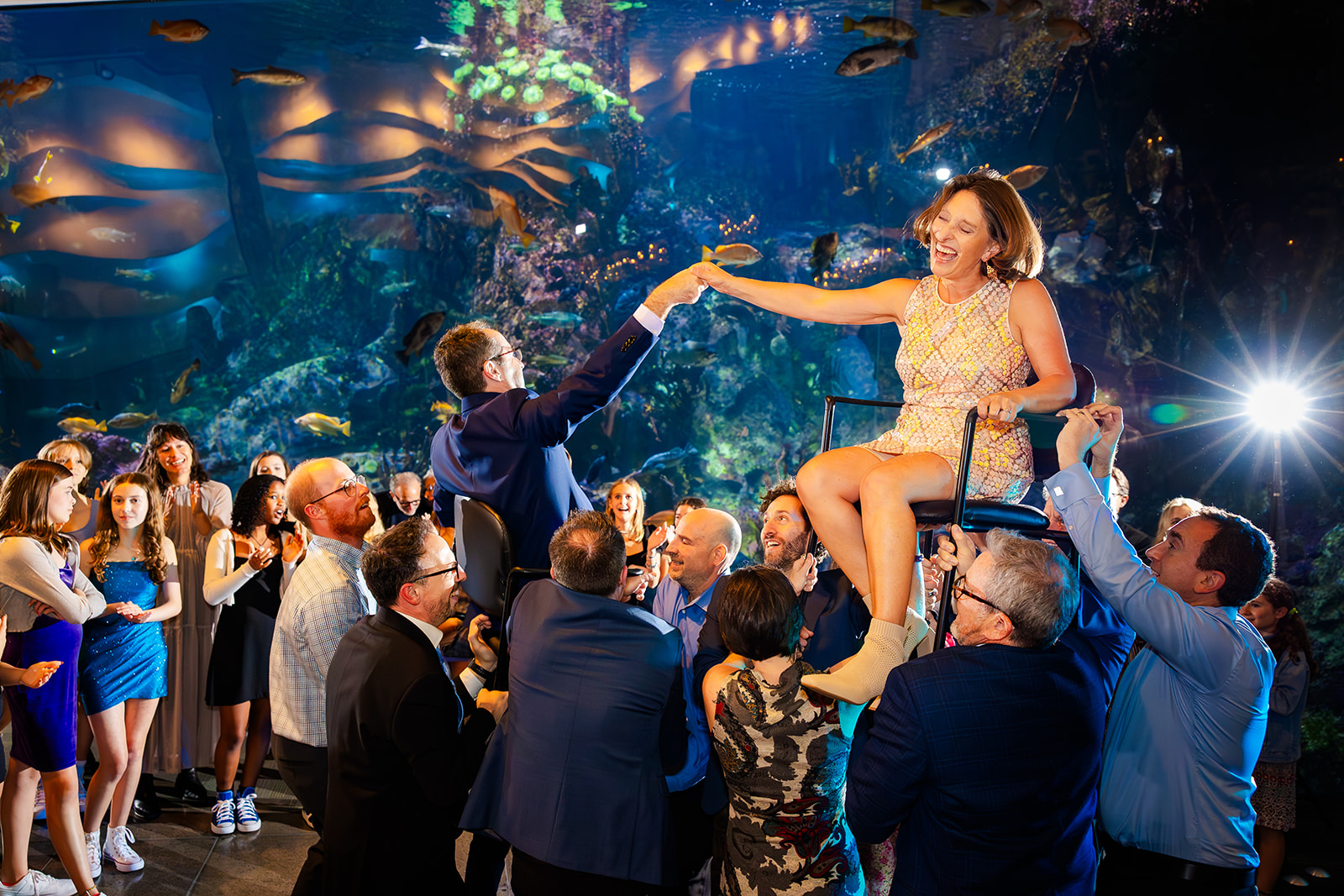 A happy mom and dad are lifted in chairs at the Aquarium while dancing at one of the Unique Event Venues in Seattle