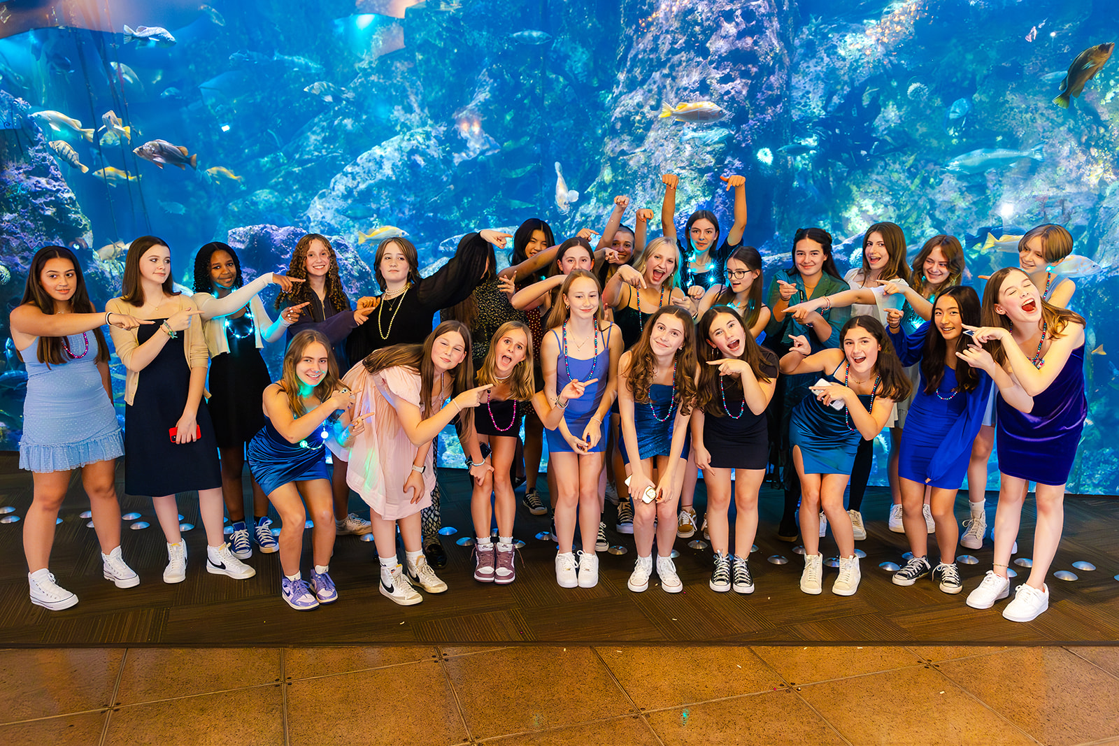 A group of girls all point to one in the center in front of a large fish tank at one of the Unique Event Venues in Seattle