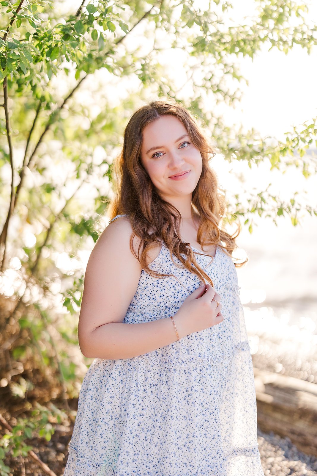 A smiling high schooler in a blue dress walks by the water twirling her hair after using Seattle Promise