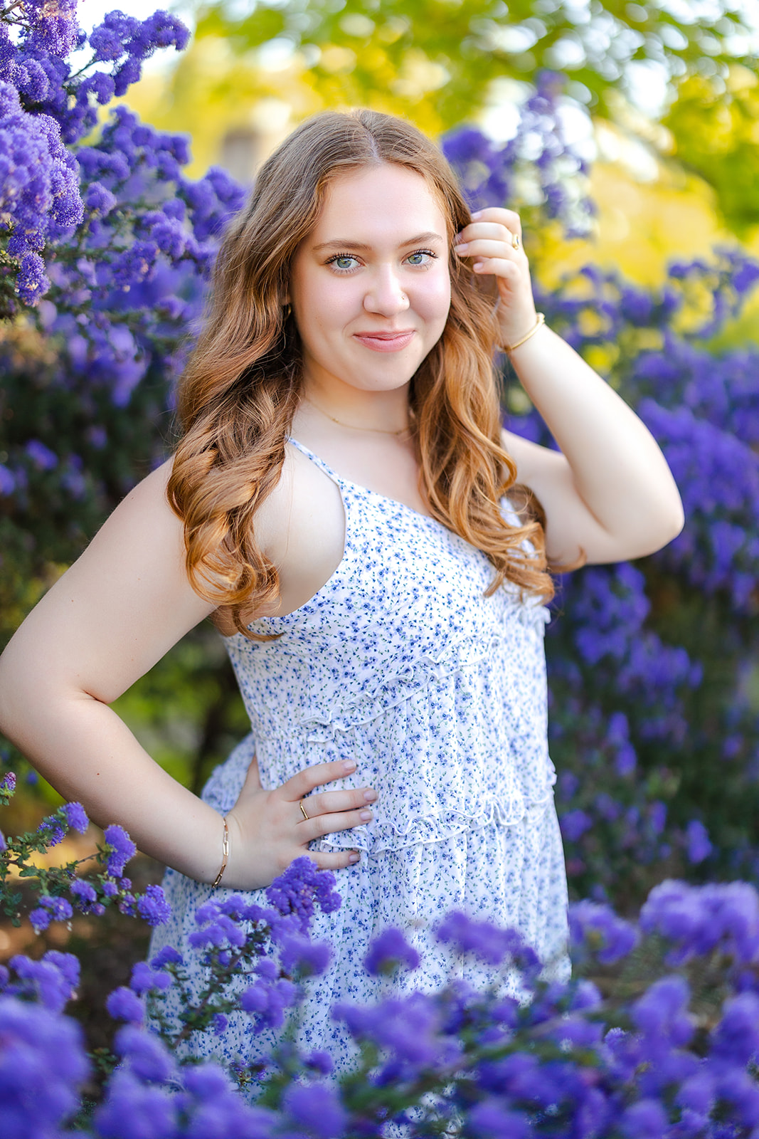 A high school senior in a blue print dress stands in a bush of blue flowers in a garden after taking advantage of Seattle Promise