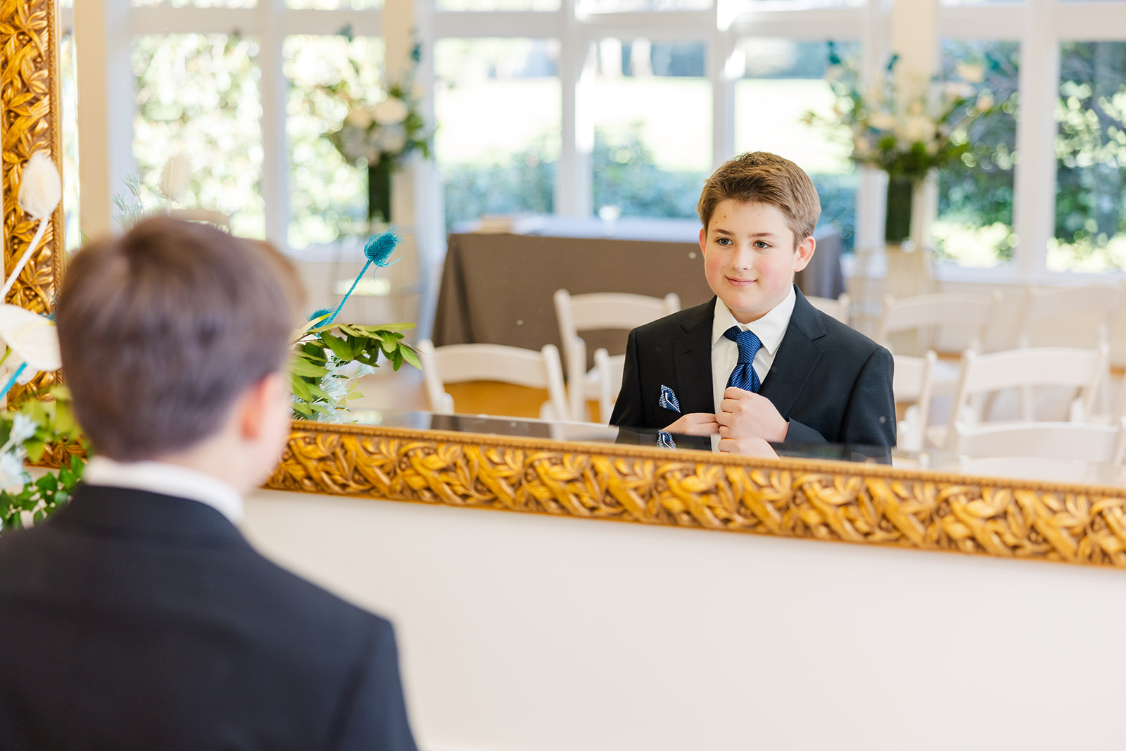 A young boy adjusts his tie in a large mirror before his Bar Mitzvah reception