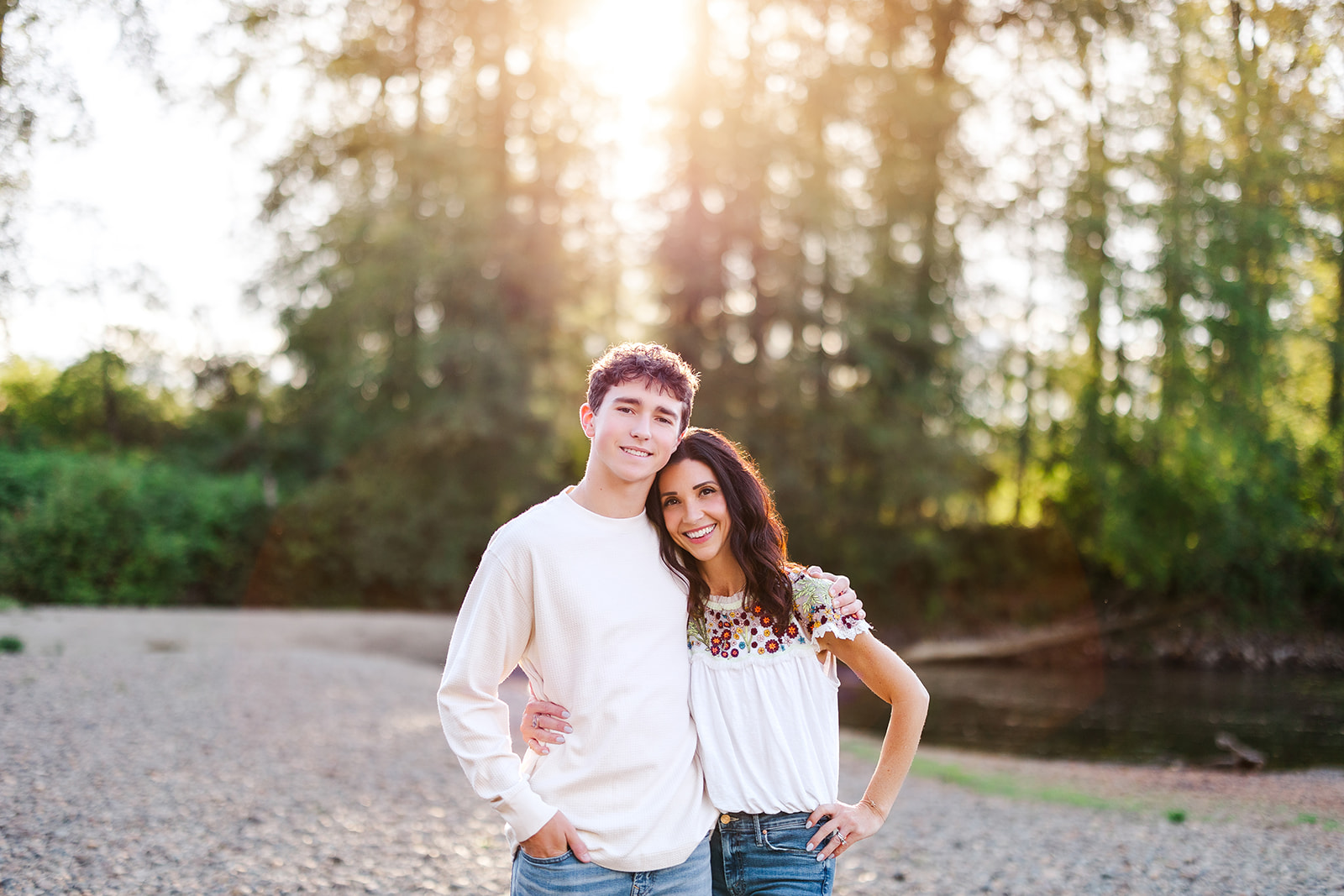 A happy mom hugs her tall high school senior son in a park by a pond at sunset