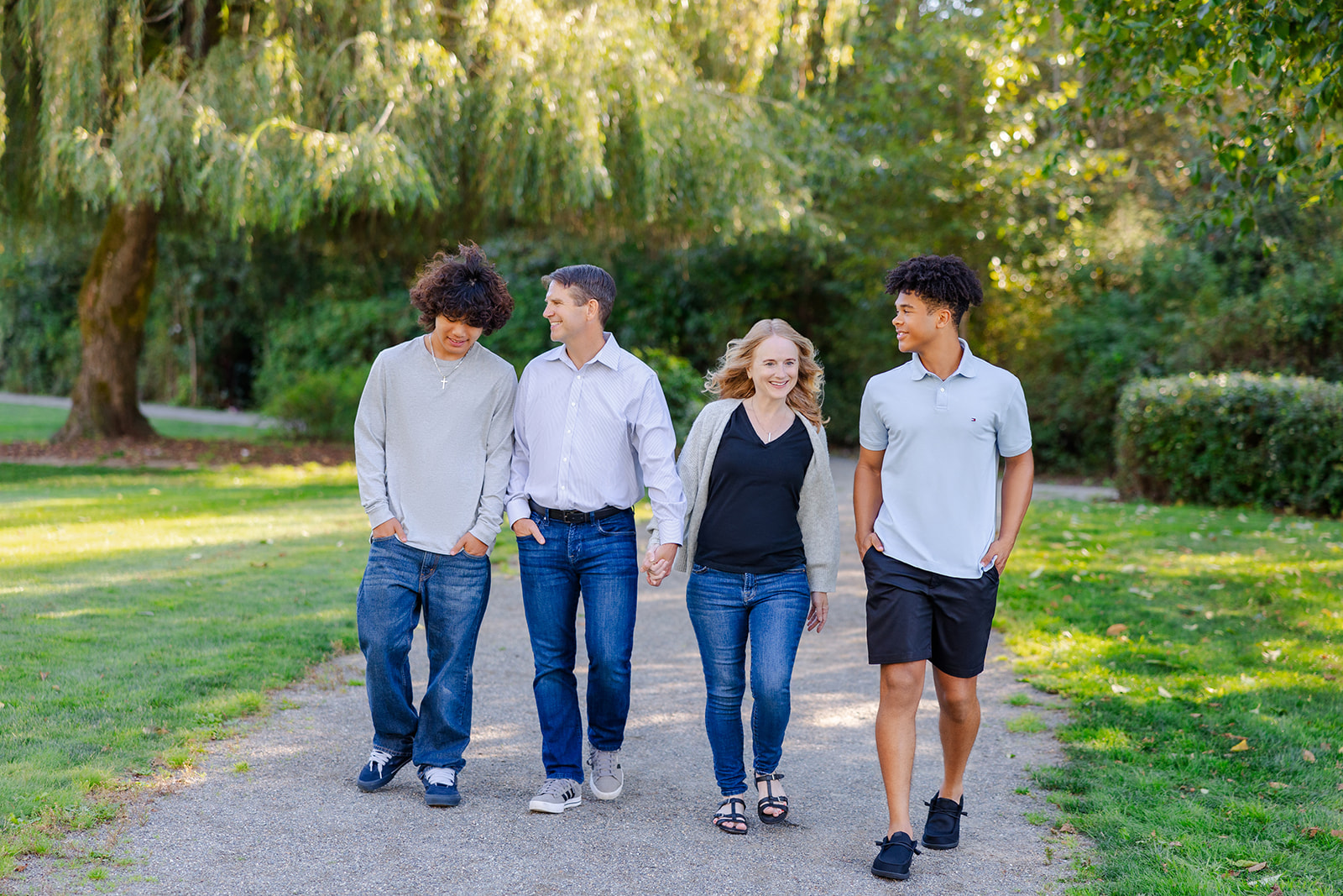 A happy family of 4 walk together in a park path in jeans and grey shirt after finding college counselors in Seattle