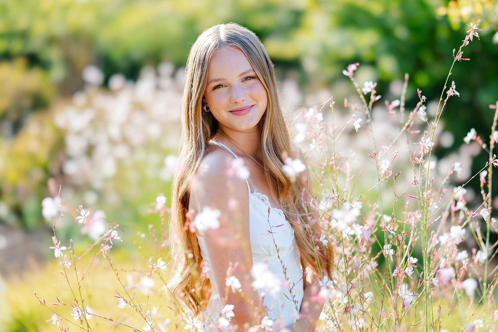 A smiling teenager in a white dress wanders in a meadow of wildflowers after visiting college fairs in Seattle